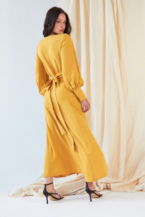 The model is wearing a Sarvin Mustard Wrap Dress.