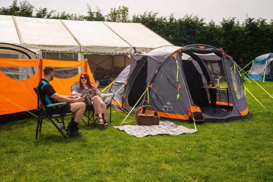 A male and female talking on a campsite near to the Abberley Xl Breeze® 4 Berth Inflatable Tent from OLPRO.