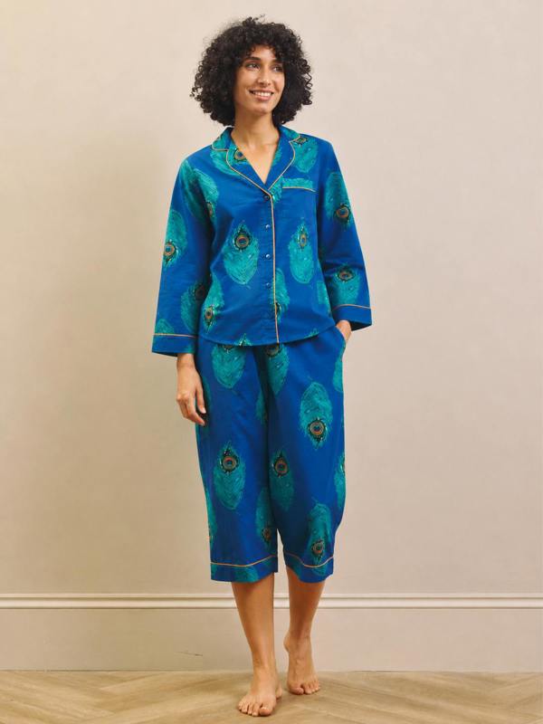 Woman wearing a blue peacock patterned capri pyjama set against a beige wall.