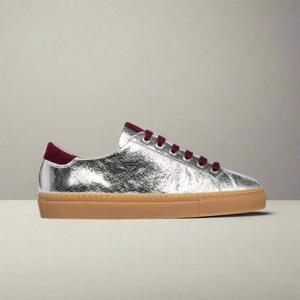 Silver sneaker with burgundy laces and sole on a light gray background