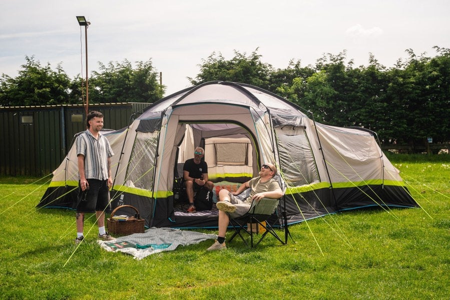 A group of males relaxing in camping furniture outside of the Hive 6 Berth Poled Tent by OLPRO