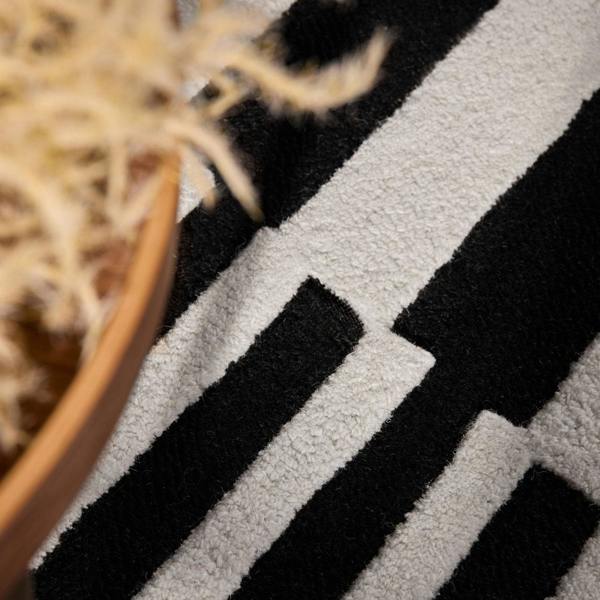 Close-up of a textured black and white rug with a plant in the corner.