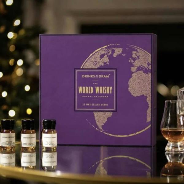 A purple World Whisky Advent Calendar styled next to three wax-sealed miniature bottles and a glass of whisky.