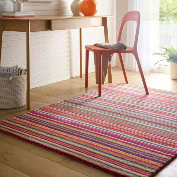 Multicolored striped rug on a wooden floor with a red chair and desk in the background.