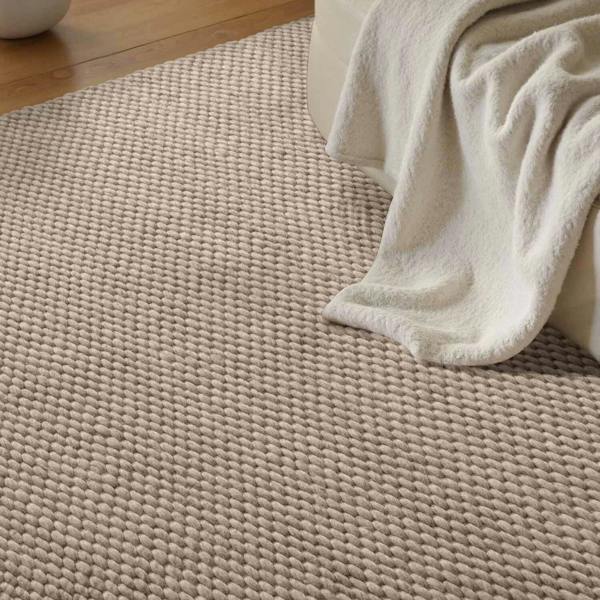 Beige woven rug with a white towel draped over it on a wooden floor.