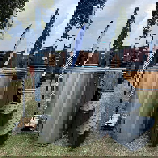 A wood-fired ofuro style hot tub with integrated heater, featuring a fibreglass liner and surrounded by wooden steps, a chimney guard, and a drinks shelf.