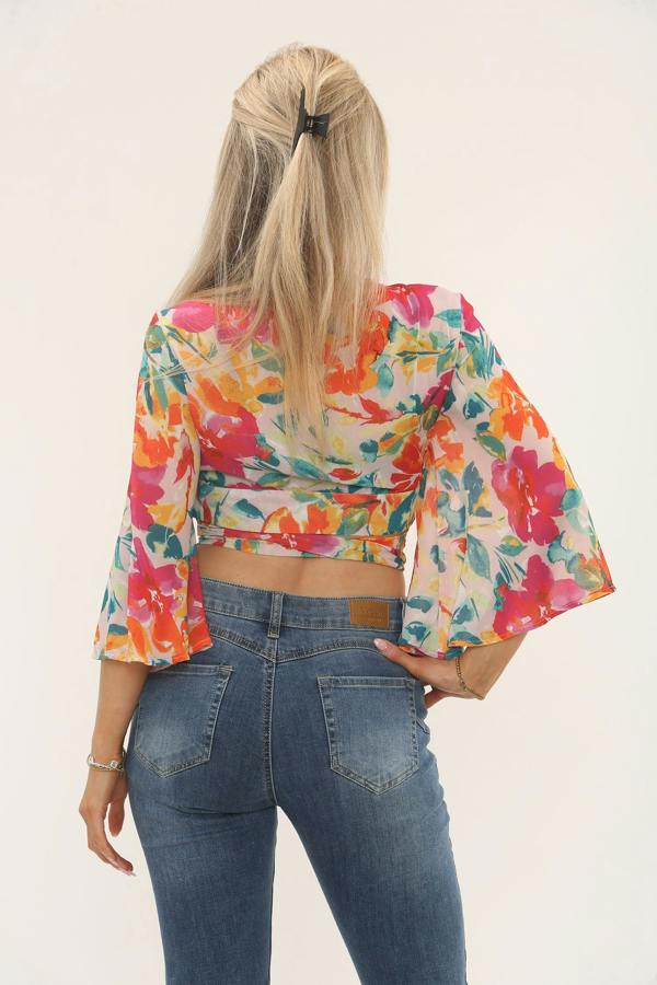 Woman wearing a bright multicolour floral wrap crop top with long flared sleeves and tie waist, styled with denim jeans, UK size 8, made from 100% polyester