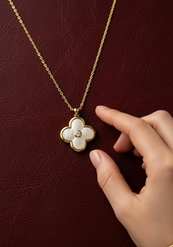Gold necklace with a clover-shaped pendant held by a hand against a dark red background