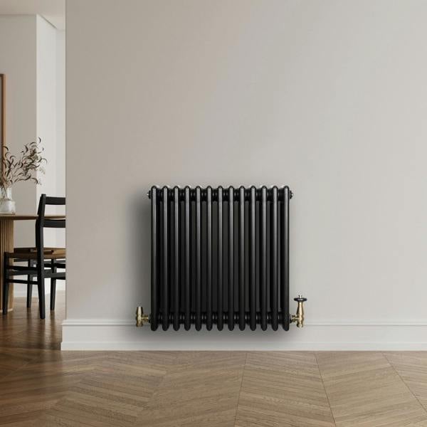 Traditional black 4 column radiator with a sleek finish, featuring brass valves, mounted on a light-colored wall in a modern room