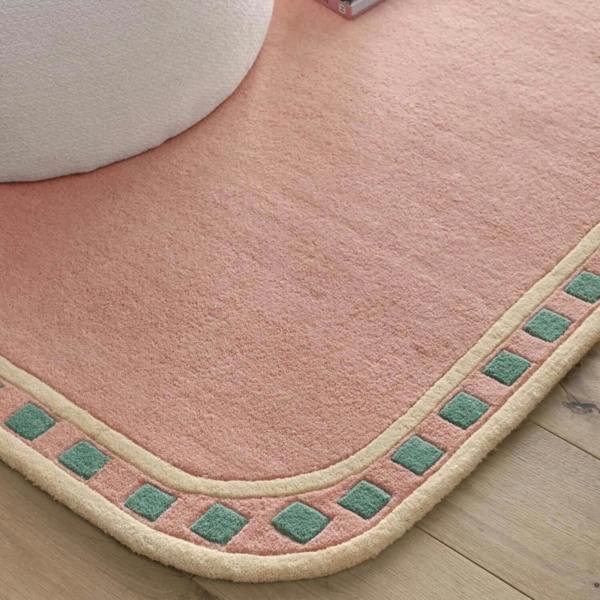 Pink bath mat with green and beige border on a wooden floor