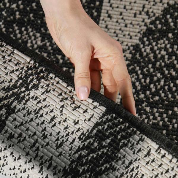 Hand touching a black and beige patterned rug