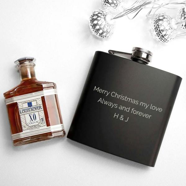 Personalised matte black stainless steel Christmas hip flask engraved with custom message next to brandy bottle