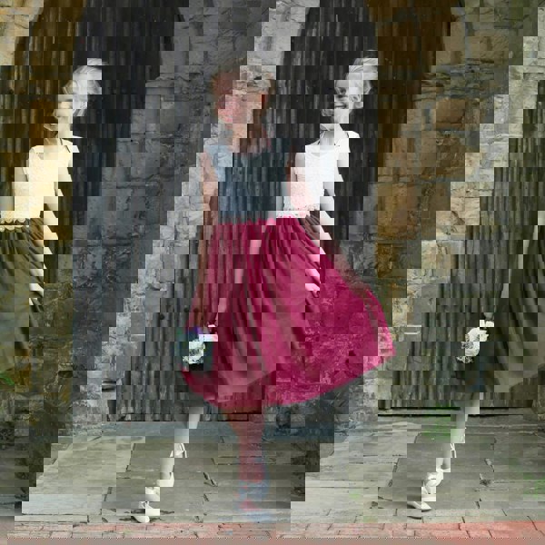 Young girl in a white top and red skirt standing in front of a stone wall.