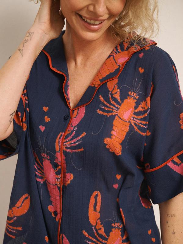 Model wearing navy gauze shortie pyjamas with a playful lobster and heart print, featuring a relaxed short-sleeve button-up shirt and matching shorts. print detail