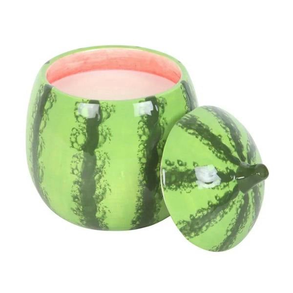 Green watermelon-shaped candle jar with lit wick; small matching lid beside.