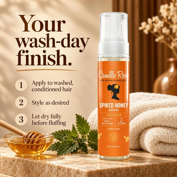 A bottle of Camille Rose Spiked Honey Mousse stands on a stone surface with a honey dipper bowl, honeycomb, herbs, and folded towels in a warm bathroom-like setting. Large text reads 'Your wash-day finish.