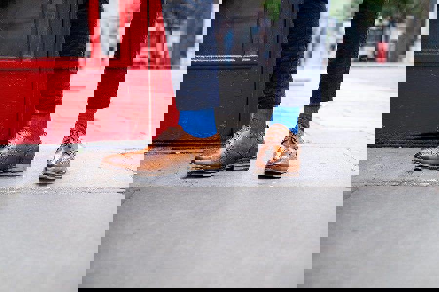 Brown leather shoes and royal blue socks worn on a sidewalk with a red door in the background