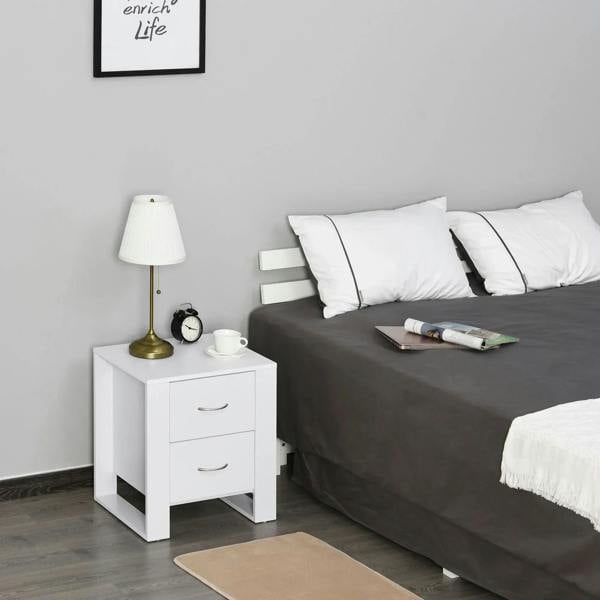 White bedside table with two drawers and curved metal handles beside a bed