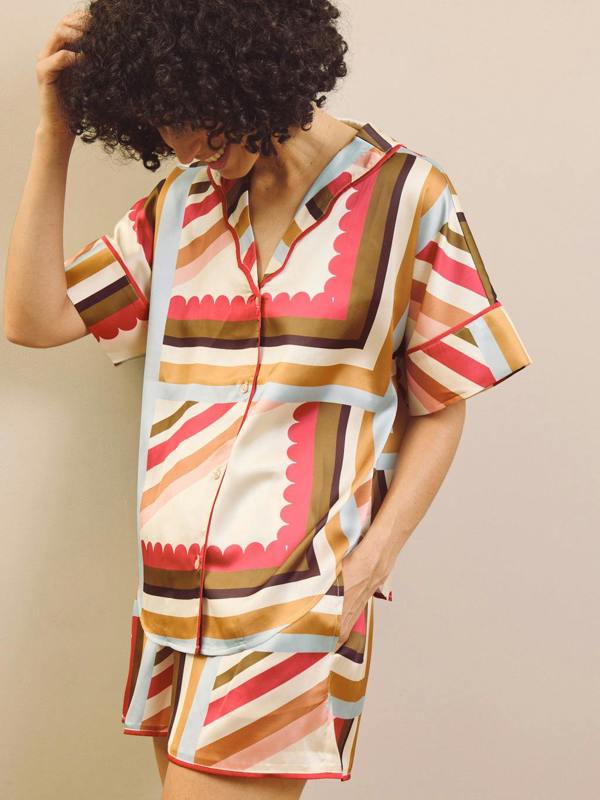 Woman wearing a colourful patterned short pyjama set against a beige background