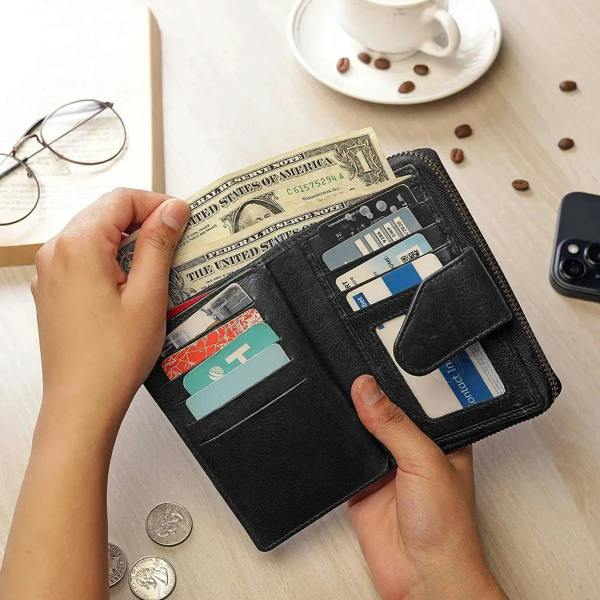 Person holding a black wallet with money and cards on a table with coffee beans and a phone.