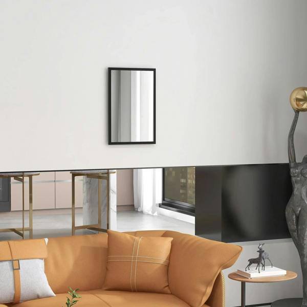 Black framed wall mirror on light wall, reflecting sofa and window light