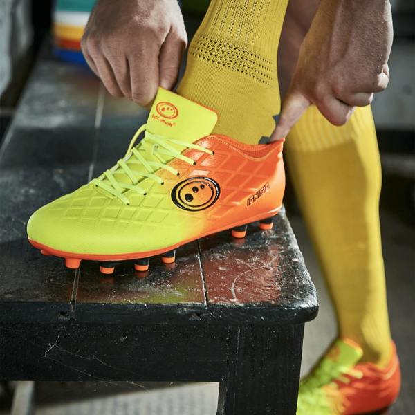 Player lacing neon yellow and orange Optimum football boot while wearing yellow knee socks, lifestyle - Optimum