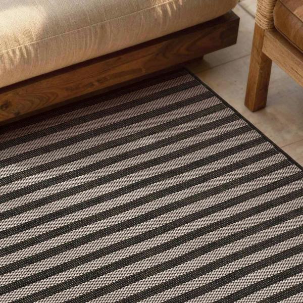 Striped black and white rug on a wooden floor with a beige sofa and wicker chair.