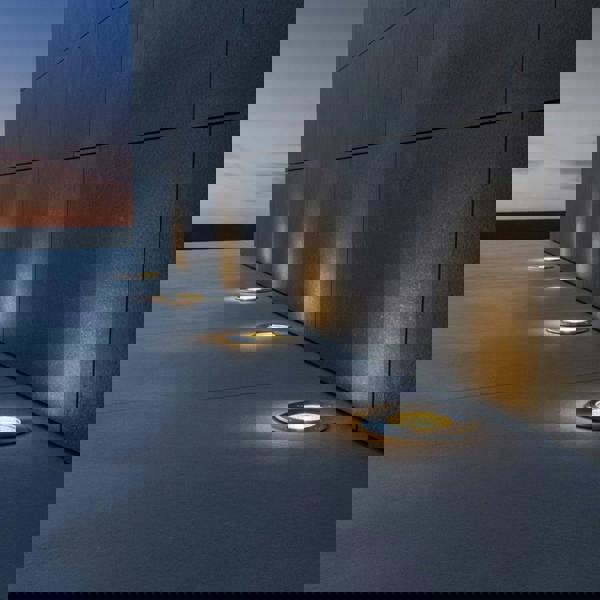 stainless steel outdoor ground lamp mounted in a row next to a wall outside