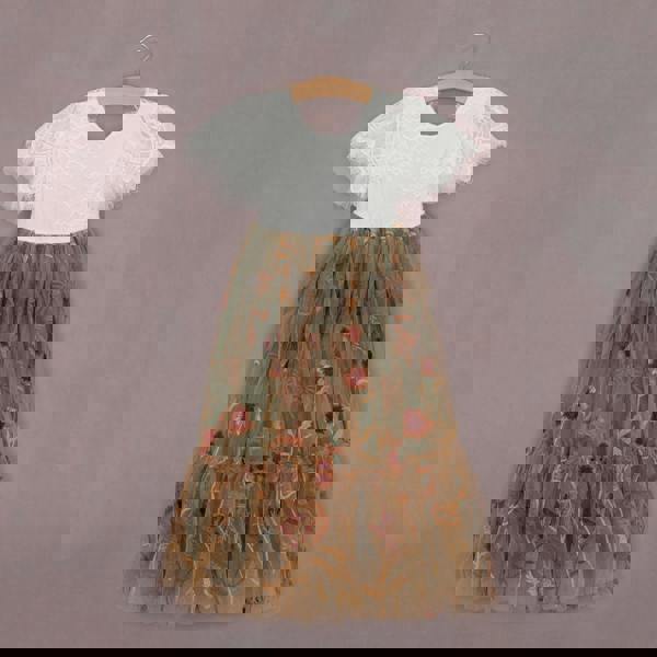 White top with lace sleeves and floral embroidered skirt on a hanger against a gray background