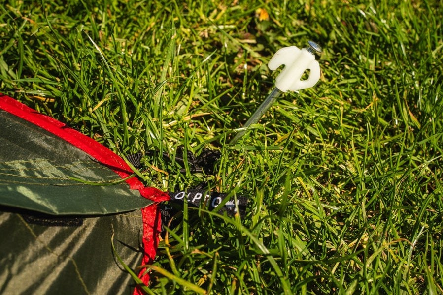 An OLPRO Glow in the Dark Peg that has been staked into the grass through the ring and pin system of the Hawford Lightweight 2 Person Tent (Ripstop).