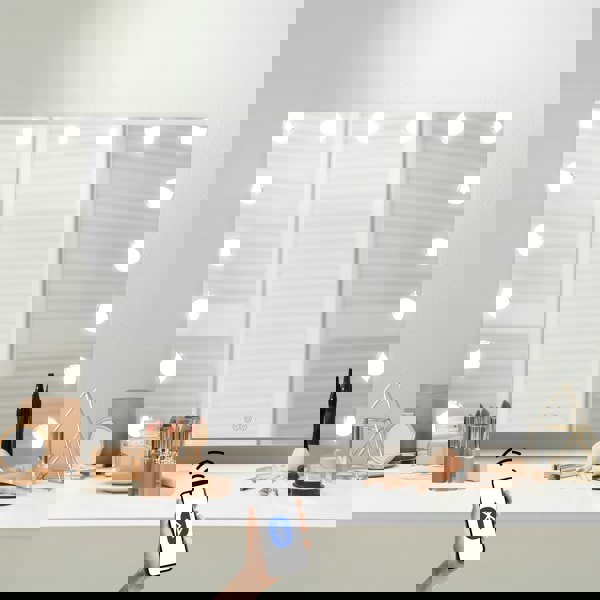 LED Bluetooth mirror 80 x 60cm with bright round bulbs, sleek glass surface, and a hand holding a smartphone for remote control