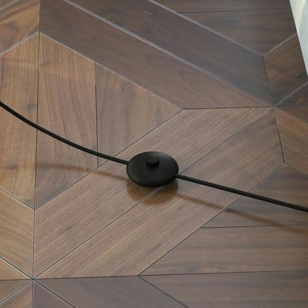Black floor lamp base with round foot and power cord on wooden floor
