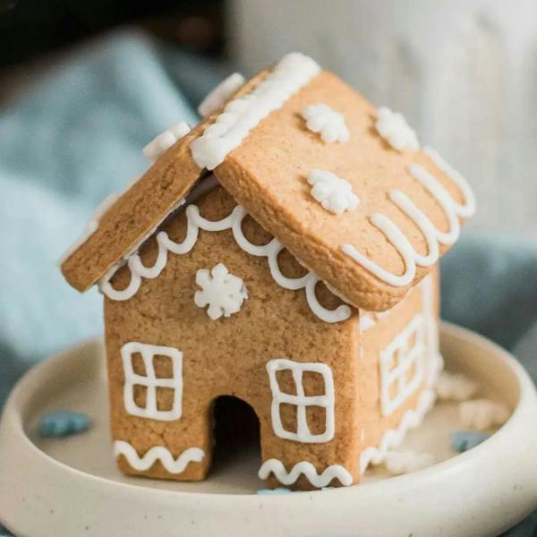 Assembled mini gingerbread house decorated with white piped icing and snowflake sprinkles, sitting on a small ceramic dish.