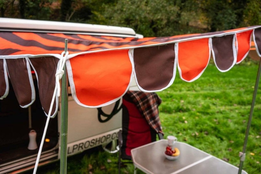 A close up of the material and poles of the OLPRO Orange and Brown Campervan Canopy that is attached to a Volkswagen Camper Van.