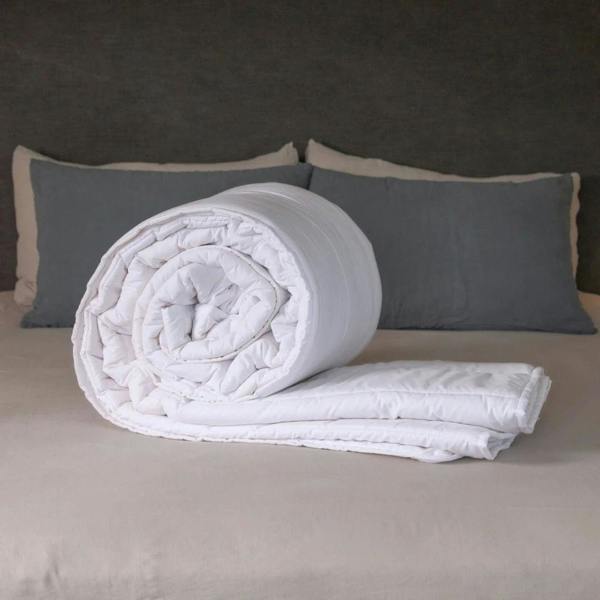 British Wool Summer Duvet 100% cotton handmade in the UK made to be hypo-allergenic, anti dust mite & sustainable. Rolled on a bed with visible cotton cover and Putnams tag, in a calm bedroom setting