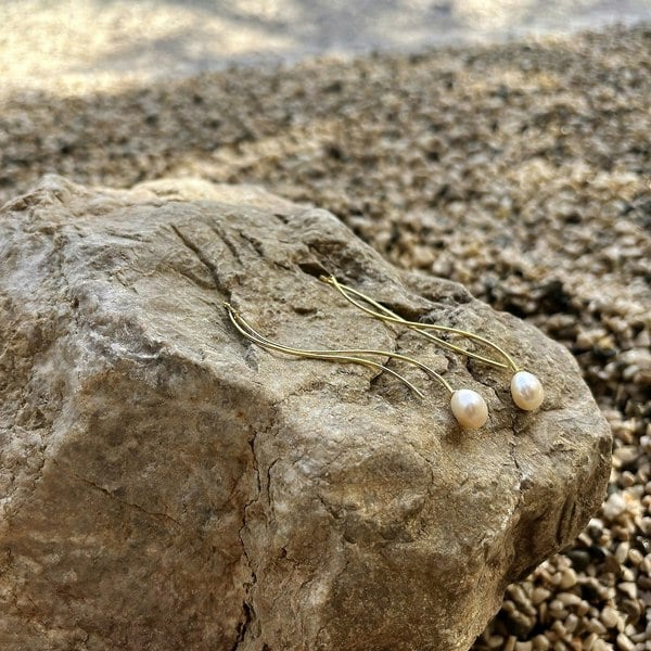 Gold vermeil long earrings displayed on a rock in beach setting.