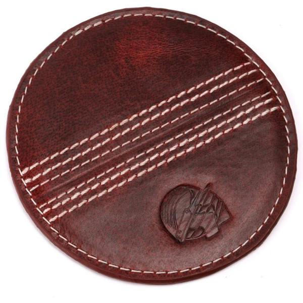 A top-down shot of a round, deep red buffalo leather coaster featuring three parallel rows of white cricket ball stitching and an embossed helmet graphic, isolated on a white background.