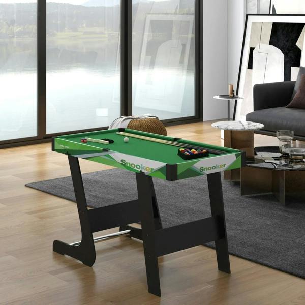 Green mini pool table set with balls and cues in front of large windows