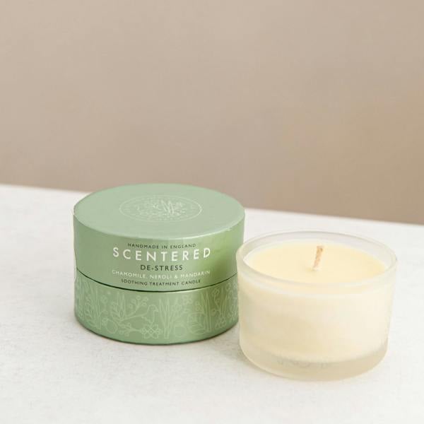 Scented candle and green gift box on a white surface.