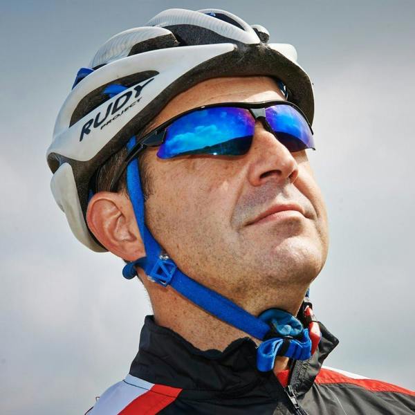Cyclist in white helmet wearing Optimum sunglasses with blue mirrored lenses against sky, lifestyle shot - Optimum