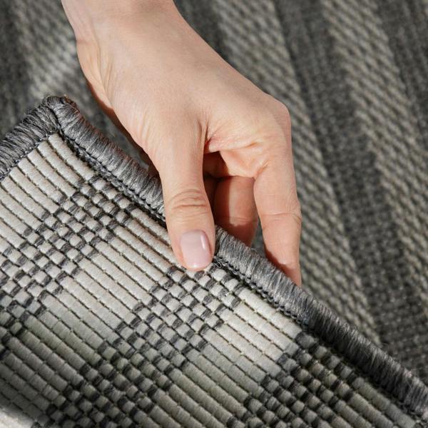 Hand holding a corner of a textured gray rug