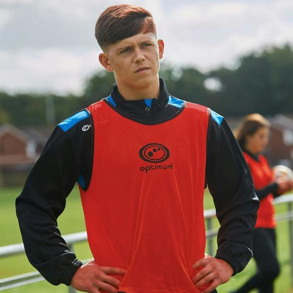 Young player wearing red Optimum training bib over black top outdoors, logo on chest, front view - Optimum