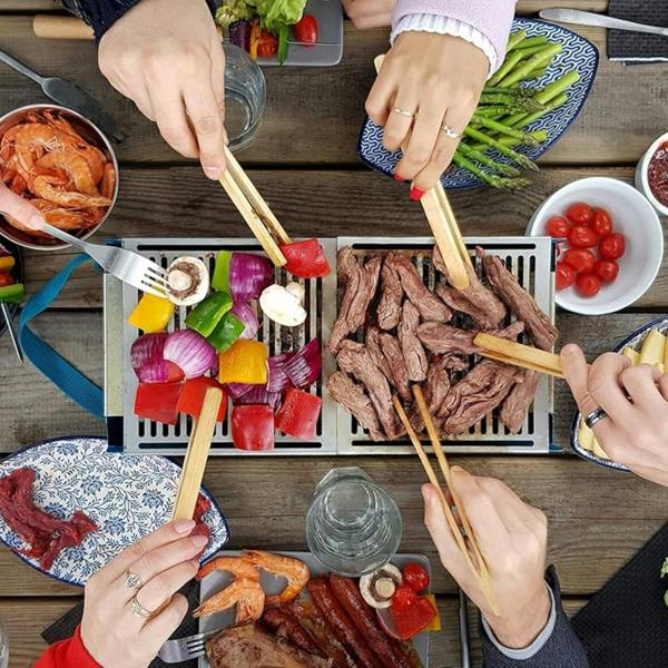 A group of friends using bamboo tongs to grill meat and vegetables on a portable Yaki BBQ.