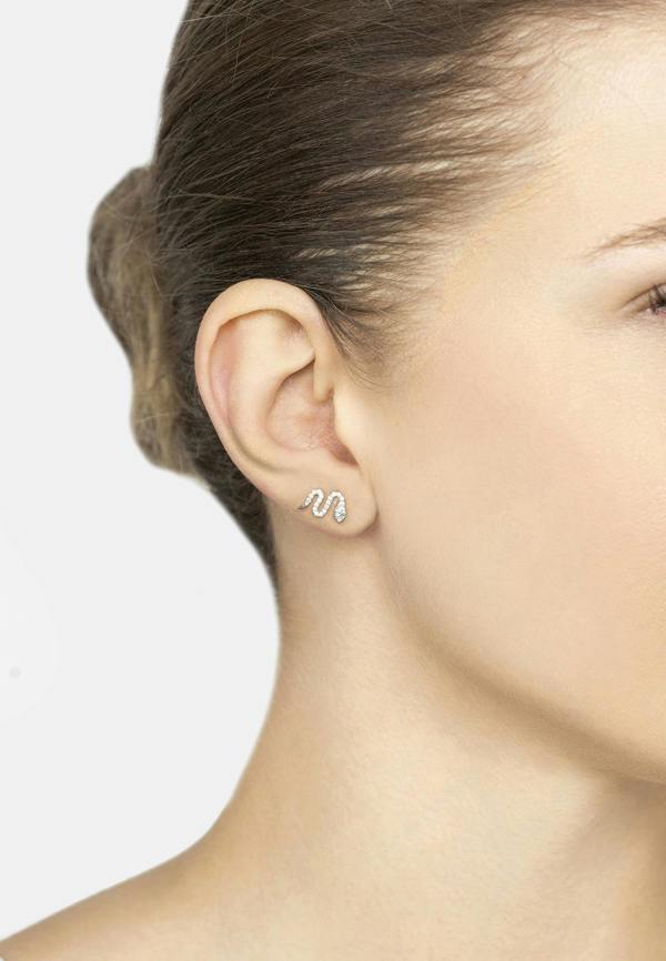 Close-up of a person wearing a snake-shaped earring on a plain background
