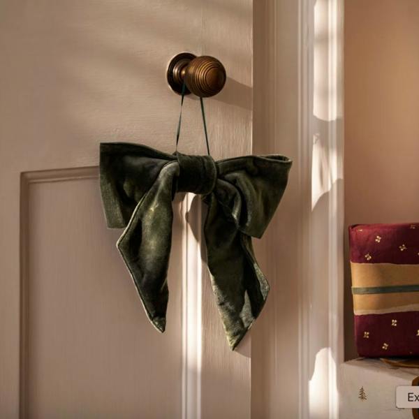 A plush fern green cotton velvet Christmas door bow with a thin hanging loop displayed against a white door.