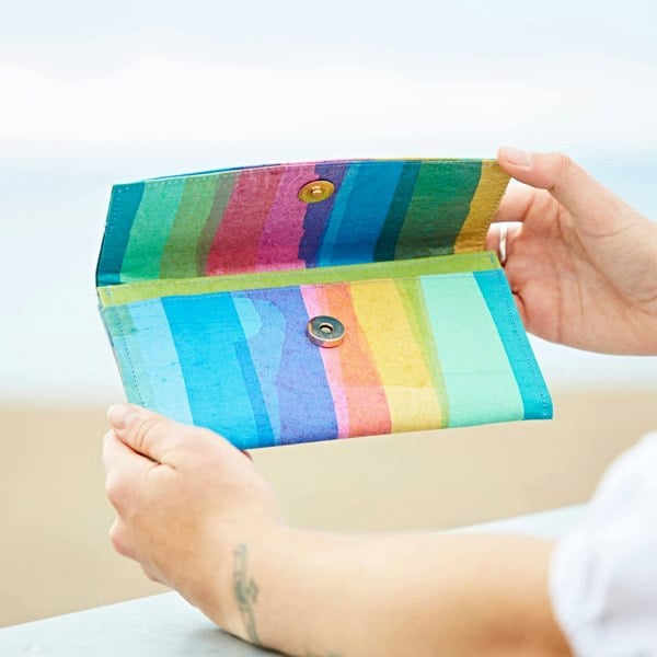 A woman holding up a Recycled Plastic Rainbow Clutch Purse on a beach made from recycled plastic.