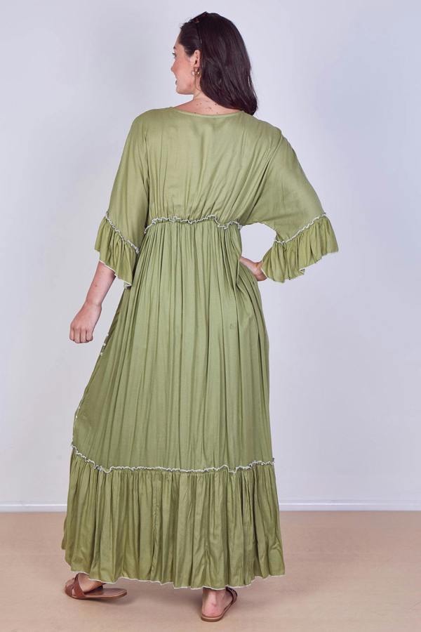 Woman wearing a green dress with ruffled sleeves and bottom hem on a plain background