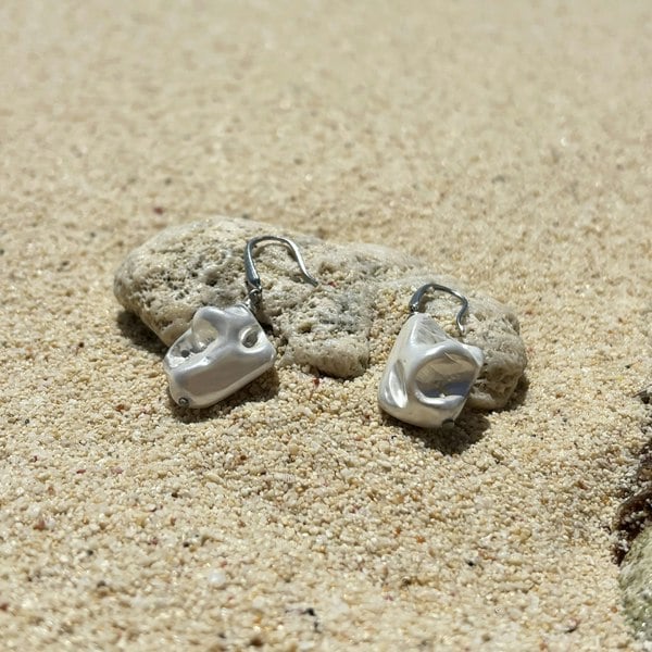 Silver shell earrings featuring rhodium-plated hooks and electroplated sterling silver natural irregular shells, shot on a beach.