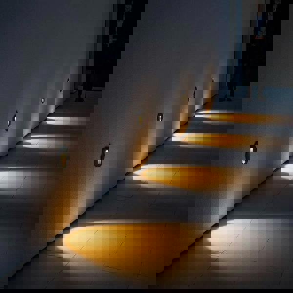 black outdoor stair step light mounted in a row along an outside wall shining light downwards