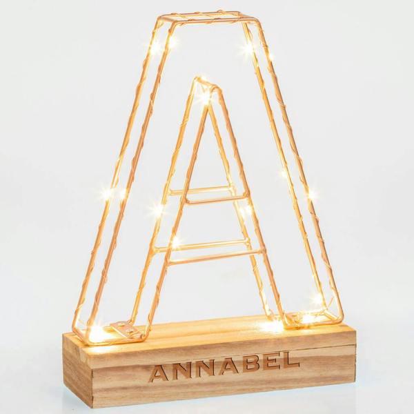 An illuminated copper wire letter A Personalised Name Letter Light with the name Annabel engraved on its solid wooden base against a bright background.